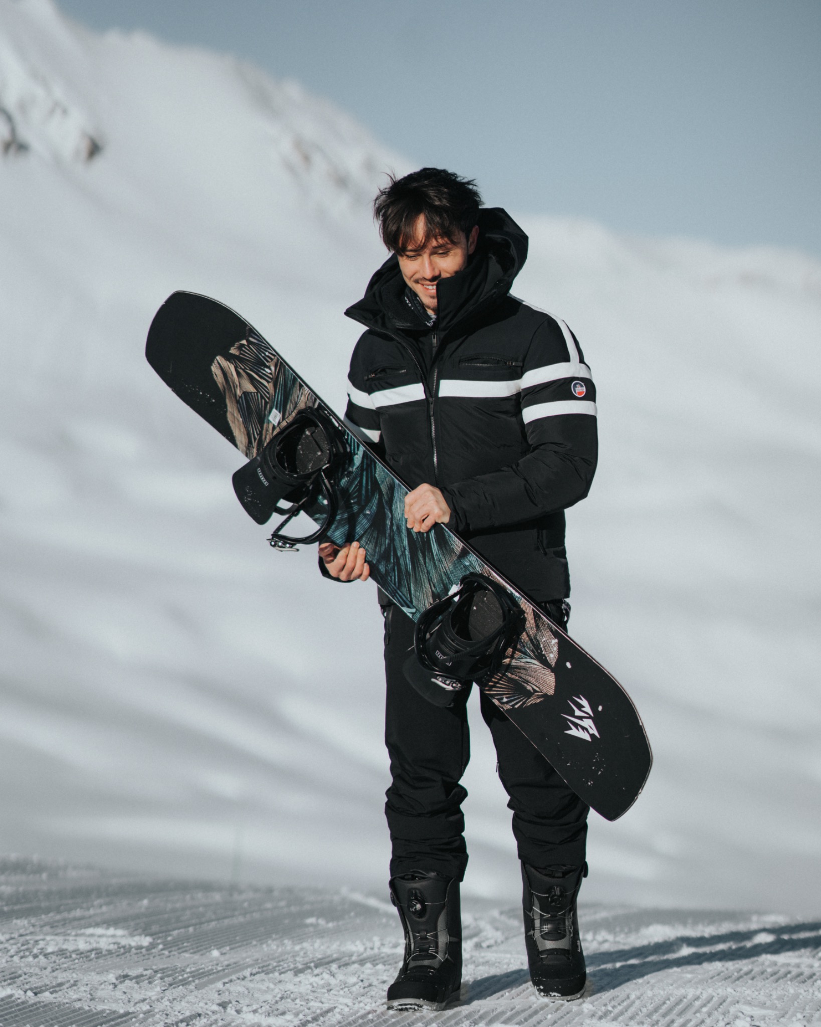 Enzo Carini holding a snowboard in the snow for Fusalp X Audi