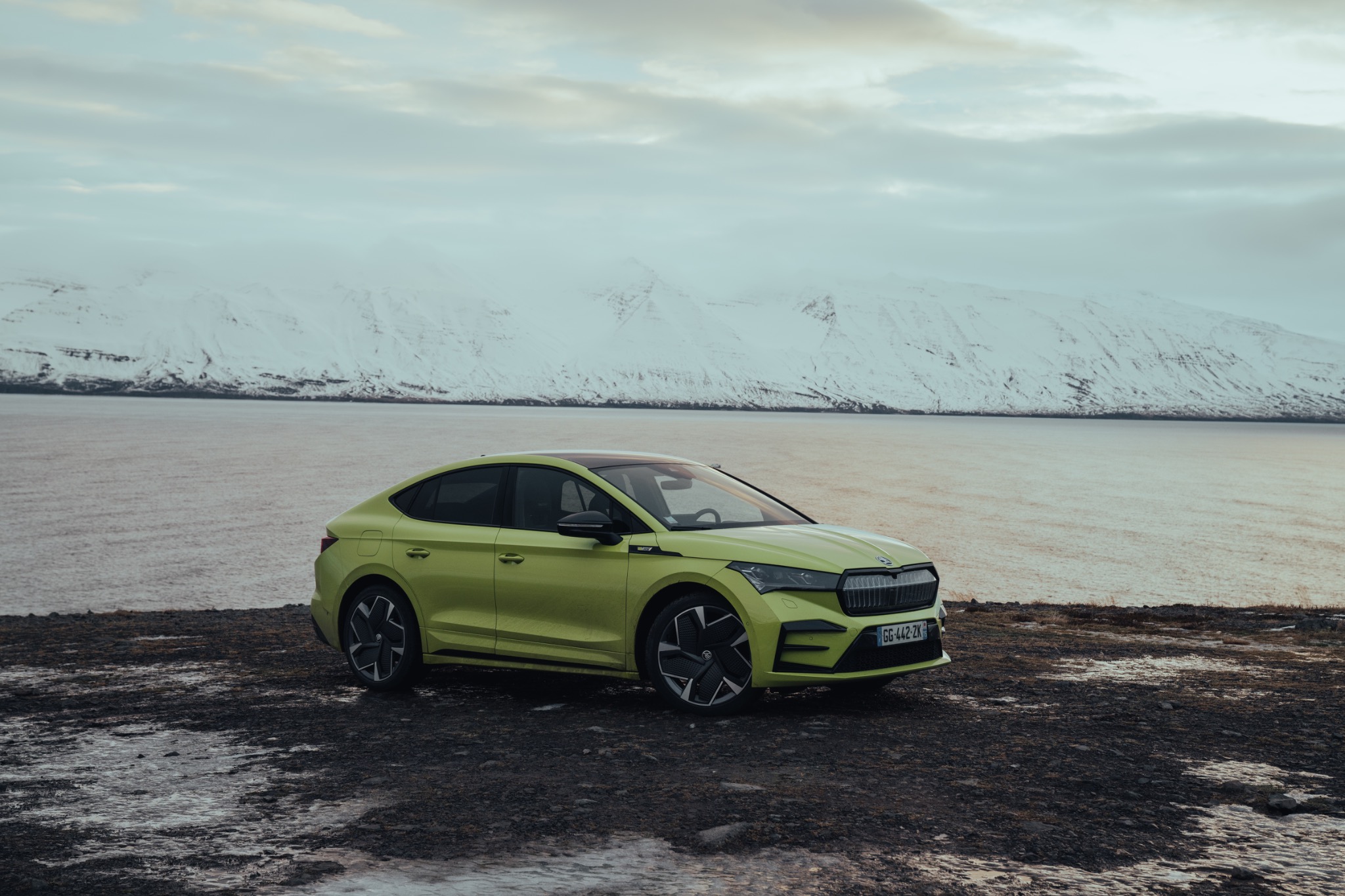 Green Skoda parked by a snowy shoreline
